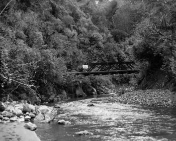 Old Bridge supporting the Orongorongo pipeline across the Orongorongo River - 1960s - Wainuiomata Historical Museum Society: L3526